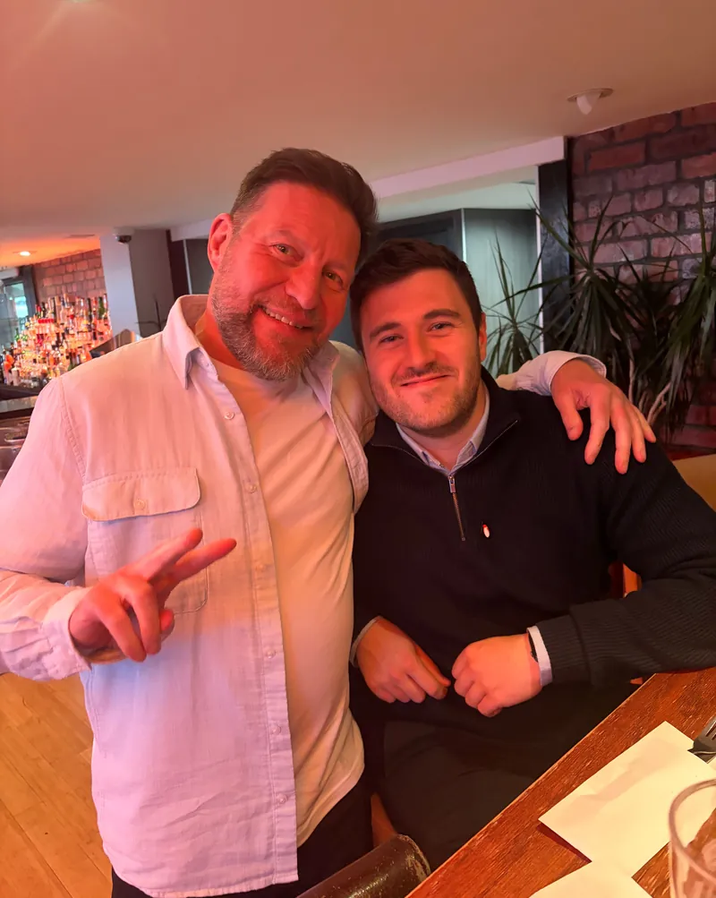 Liam, on the right, smiling for a photo at a bar with a man making a peace sign
